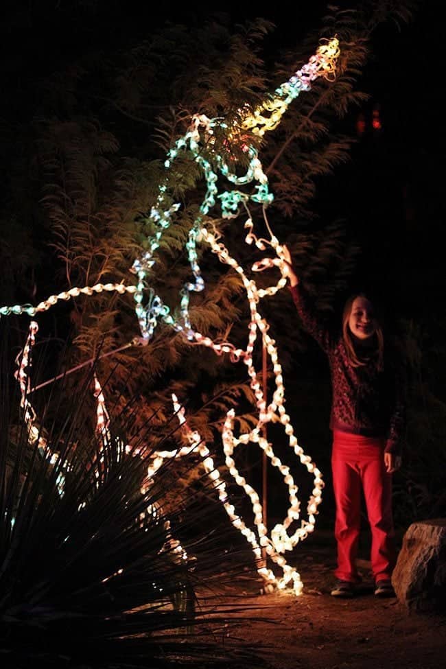 little girl standing on the side of unicorn figure with light