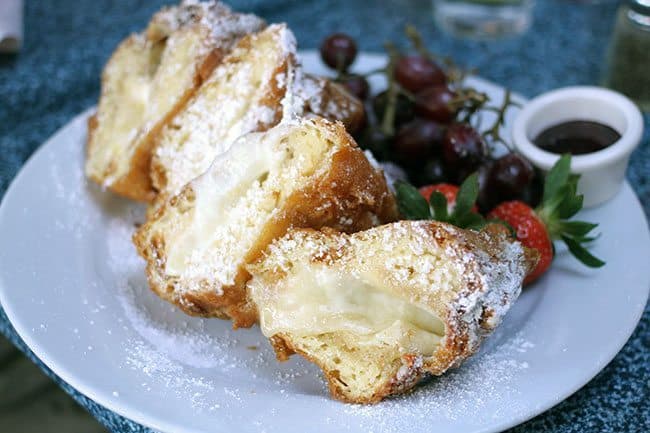 Four Slices of Three Cheese Monte Cristo in a white Plate with Fruits on the side