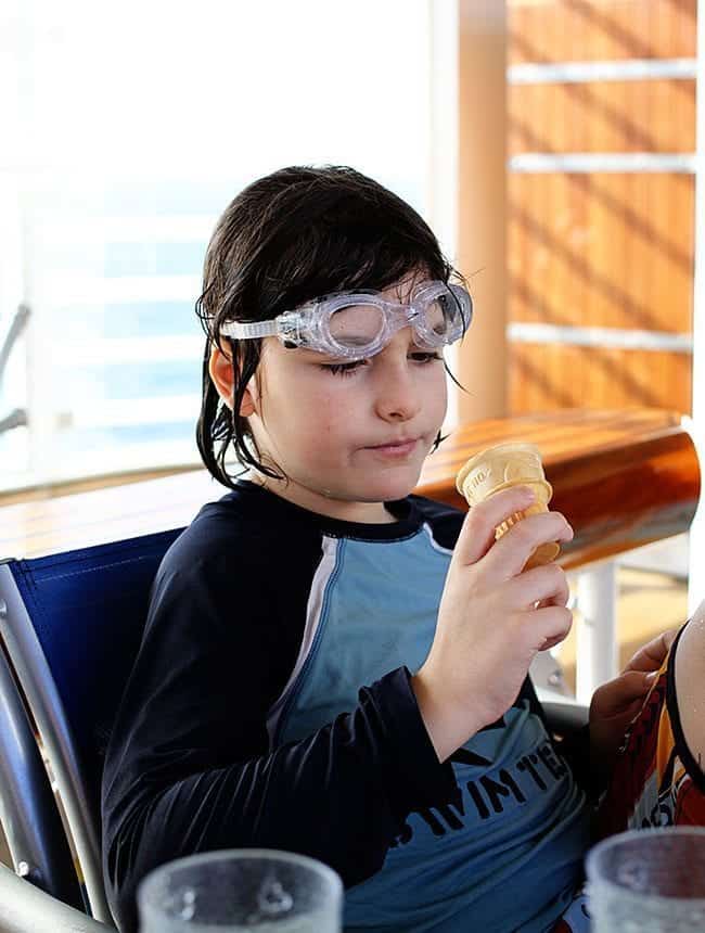 a kid wet from swimming, sitting and holding an ice cream cone