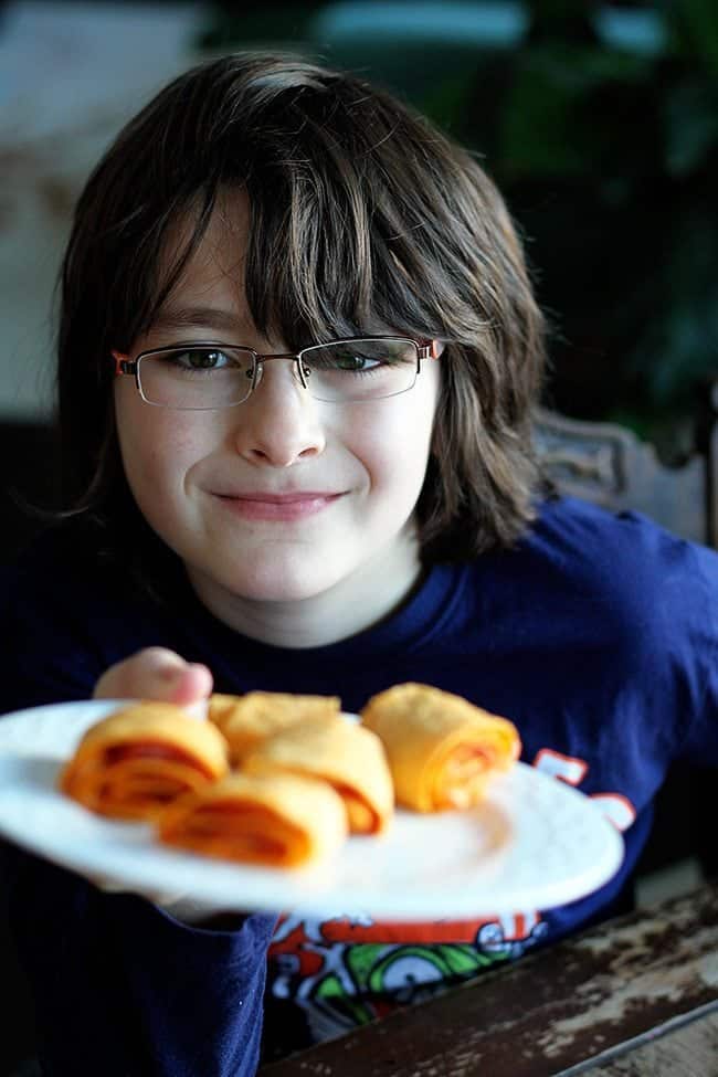 A boy wearing blue shirt holding a plate with Pepperoni Pizza Rolls