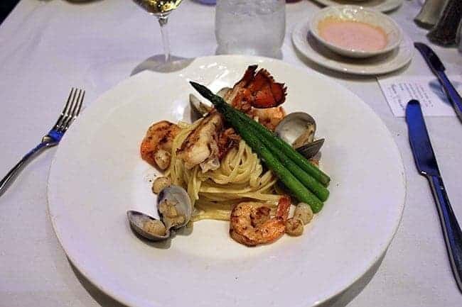 white plate with seafood pasta with a lobster tail, scallops, mussels and shrimp
