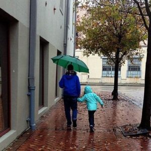 Father and his child walking under the rain with green umbrella