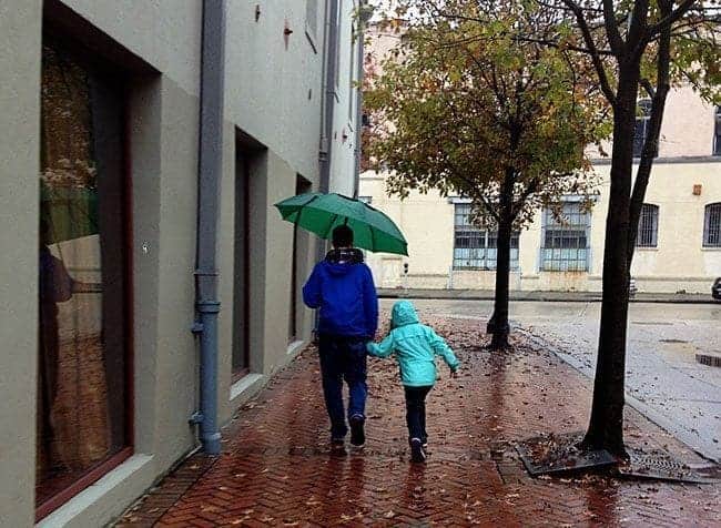 Father and his child walking under the rain with green umbrella