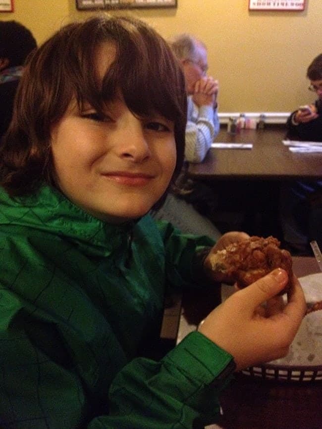 young boy holding a piece of crispy hot chicken at Willy Mae's Restaurant