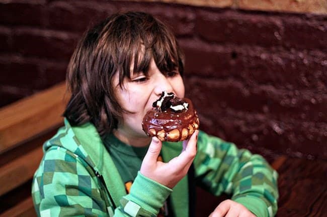 young boy having a bite of his chocolate blackout donut