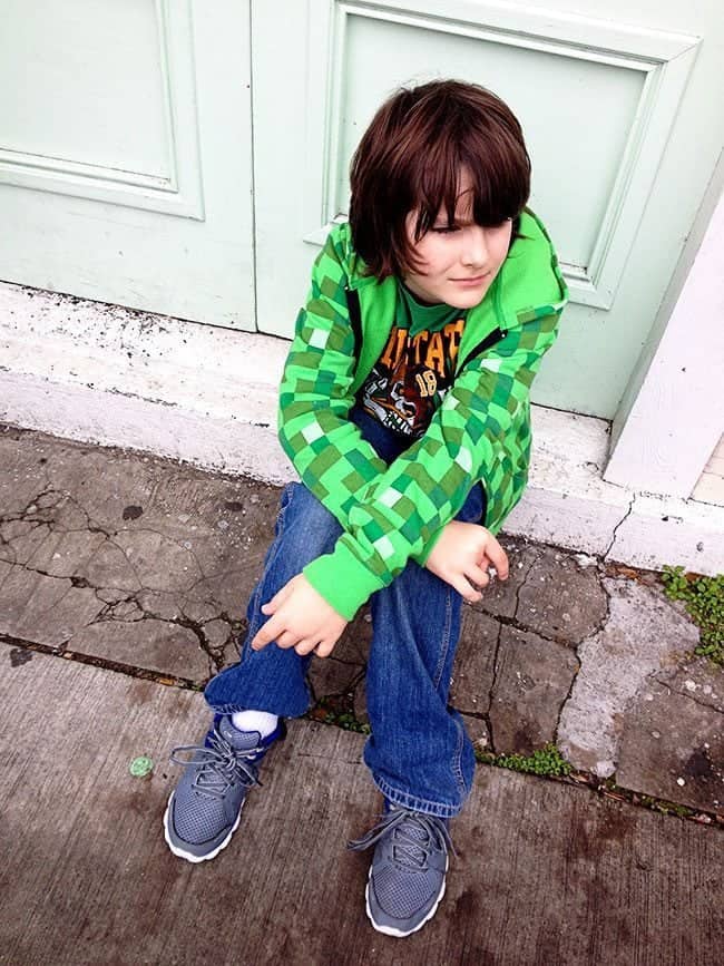 young boy wearing green shirt and jacket sitting near the door
