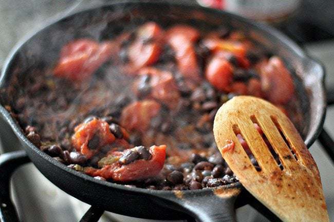 Cooking beans, tomatoes and cumin in skillet