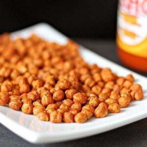Roasted Chickpeas in a white rectangular plate and a bottle of Buffalo Hot Sauce