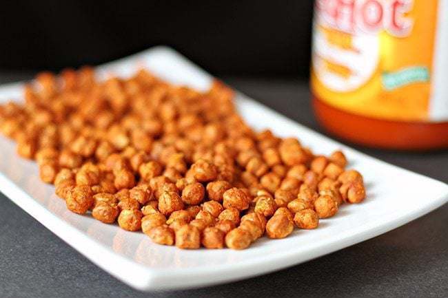 Roasted Chickpeas in a white rectangular plate and a bottle of Buffalo Hot Sauce
