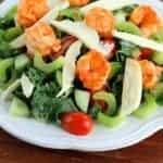 Buffalo Shrimp Kale Salad in white plate topped with celery, cucumber and tomatoes