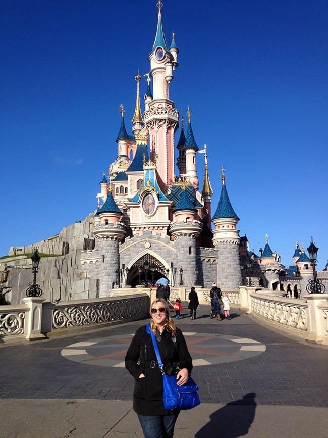 woman wearing black coat and sunglasses standing near the entrance of Fantasyland at Disneyland Paris