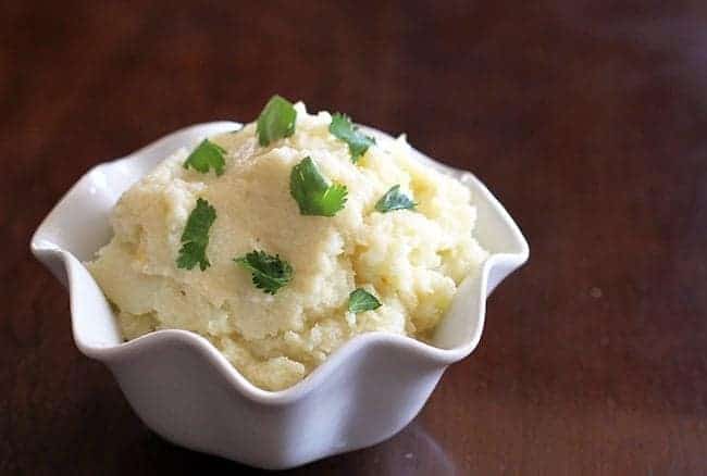 Simple & Fast Cheesy Mashed Cauliflower in a small white ruffle bowl on shiny wood background