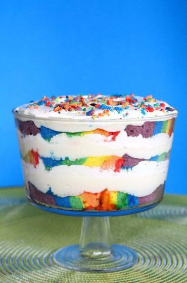 a cup of Rainbow Cake Trifle topped with whipped cream and left over rainbow cake crumbs