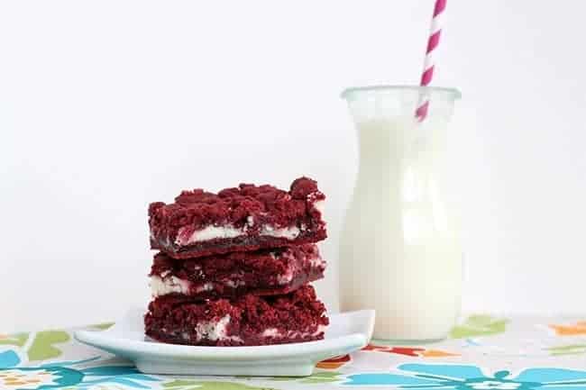 Slices of Cream Cheese Filled Red Velvet Cake Bars in a White Square Plate. A Jar with milk at the back