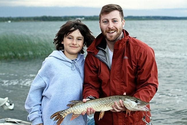 young boy beside his father holding a fish