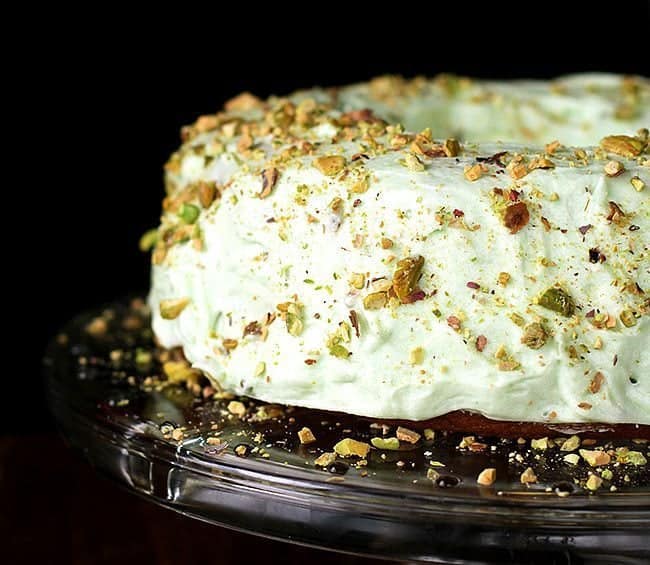 Close up of Homemade Pistachio Pudding Cake with Pistachio Buttercream Frosting in transparent cake holder