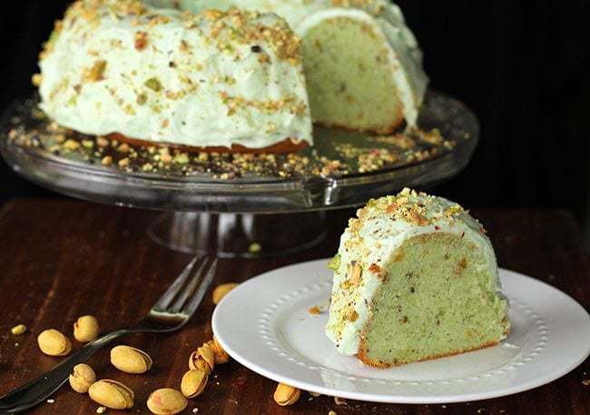 Close up of Homemade Pistachio Pudding Cake with Pistachio Buttercream Frosting in transparent cake holder and a slice in white plate