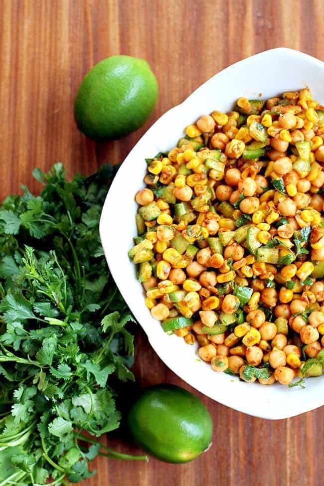 Top down shot of Roasted Corn & Chickpea Salad on a white square bowl, a bundle of Cilantro beside it