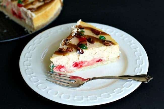 slice of vanilla cheesecake with shortbread crust with green and red cherries in a white plate