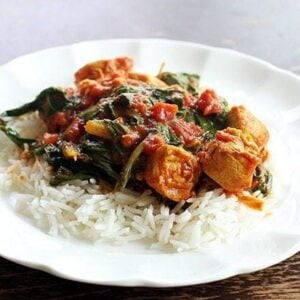 close up of Rice topped with Curried Chicken With Wilted Swiss Chard on a white plate