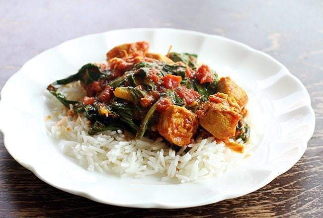 close up of Rice topped with Curried Chicken With Wilted Swiss Chard on a white plate