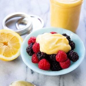 Lemon curd on a glass container and on top of raspberries and blackberries in a small Pyrex bowl