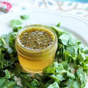 white plate with chopped green leaves and Homemade Herb Vinaigrette in a container at the center