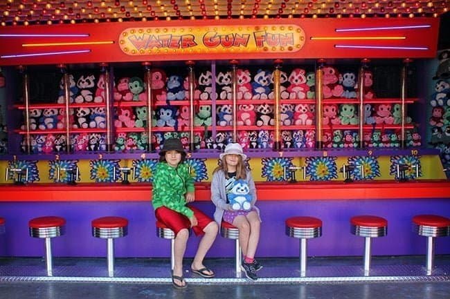 two kids sitting in front of water game fun booth holding her prize stuffed panda