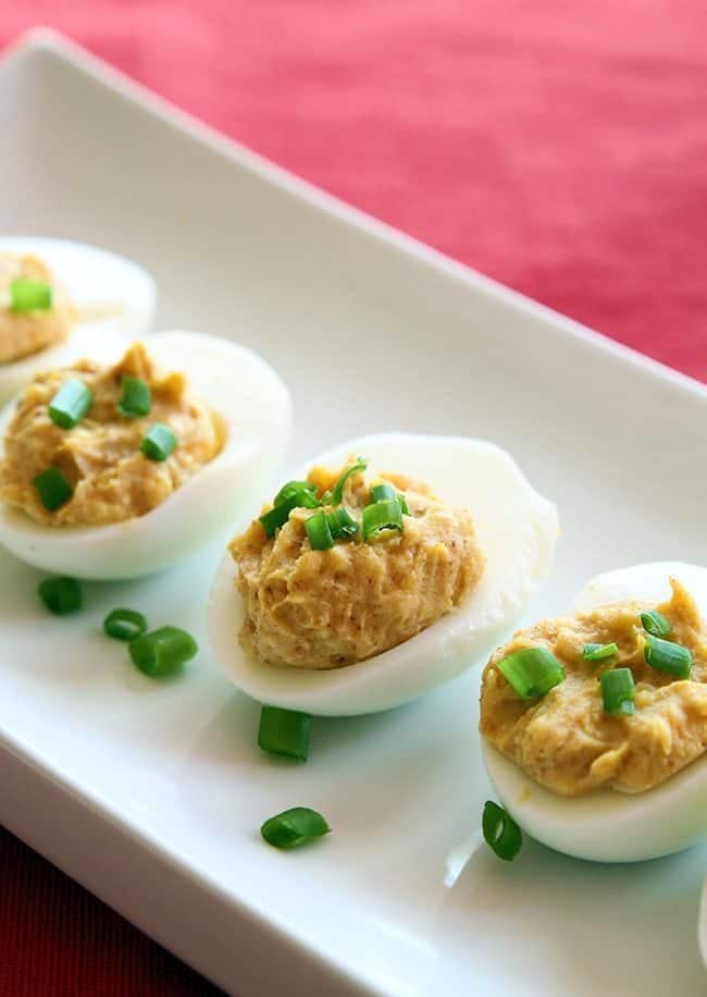 close up Curried Deviled Eggs garnish with chopped green onions in a rectangular white plate