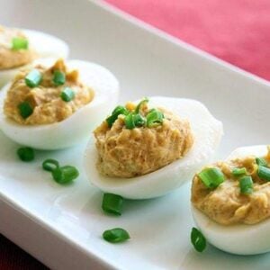 close up Curried Deviled Eggs garnish with chopped green onions in a rectangular white plate