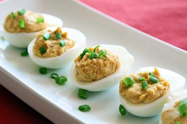 close up Curried Deviled Eggs garnish with chopped green onions in a rectangular white plate