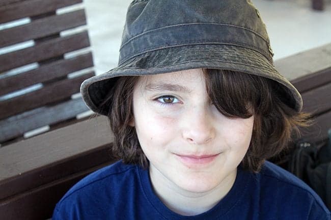 close up of young boy wearing a black cap, sitting in wooden bench