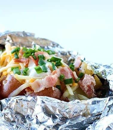 close up Campfire Grilled Loaded Baked Potatoes in a tinfoil topped with onion, cheese, sour cream, salt and pepper