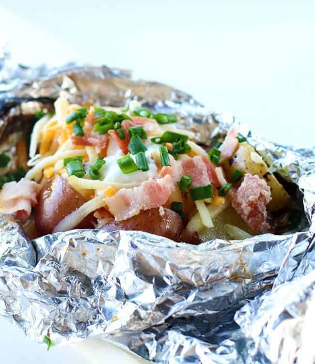 close up Campfire Grilled Loaded Baked Potatoes in a tinfoil topped with onion, cheese, sour cream, salt and pepper