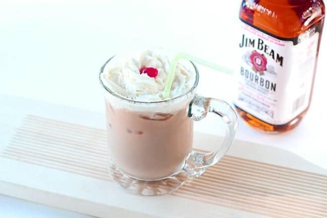 A glass of Bourbon Paralyzer topped with whipped cream and cherry. A bottle of Jim Beam brand bourbon at the back.