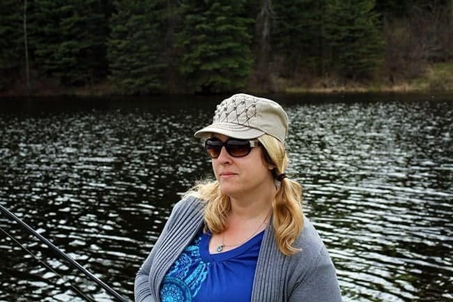 woman holding a fishing rod wearing sunglasses and cap with the background of lake