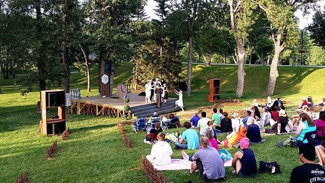 families sitting in the picnic area of the park watching the play at the stage