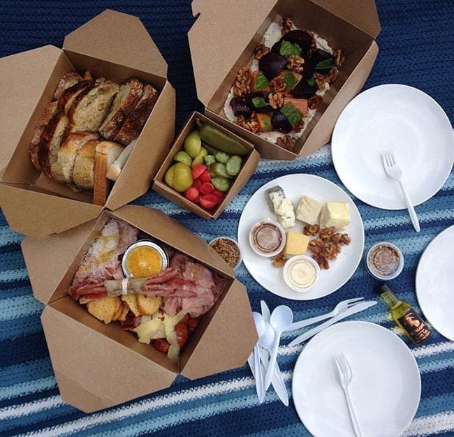 boxed foods, fruits and white plate in a picnic matt