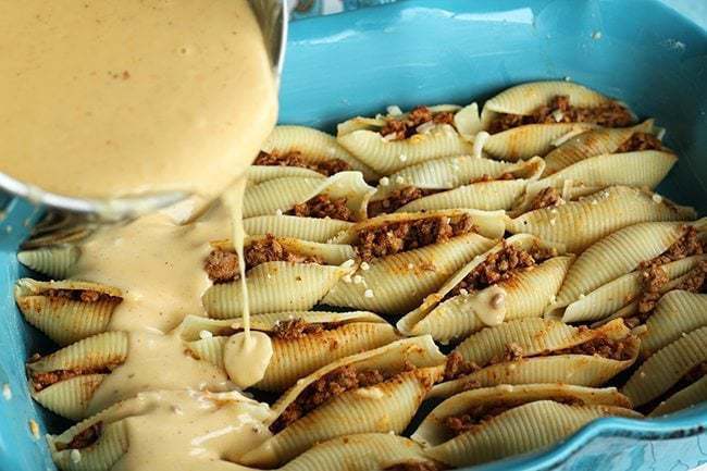adding taco cheese sauce over those stuffed little shells in baking pan
