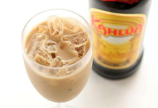 A glass of White Leprechaun Cocktail and a bottle of Kahlua on white background