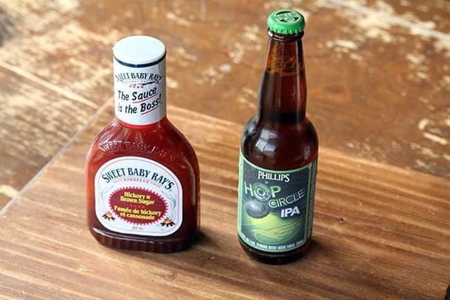 bottle of Sweet Baby Ray's brand hickory and brown sugar sauce and a bottle of strong beer on wood board
