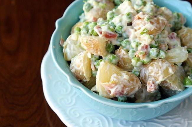 Baby Potato & Pea Salad With Garlic Bacon Aioli in blue bowl on brown wood background