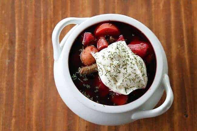 top down shot of chunky Ukrainian Borsch topped with sour cream and dill in a pot like white bowl