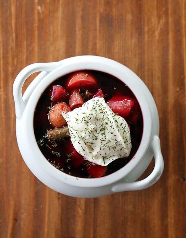 top down shot of chunky Ukrainian Borscht topped with sour cream and dill in a pot like white bowl