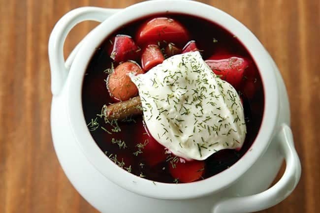 close up of chunky Ukrainian Borscht topped with sour cream and dill on brown background