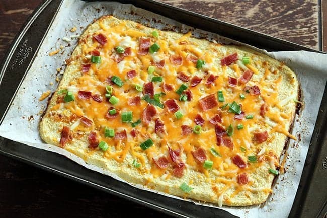 baked cauliflower mixture in a baking sheet topped with cheese, onions and bacon