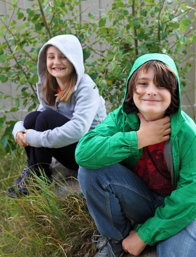 young kids sitting outside with the young boy grabbing his throat