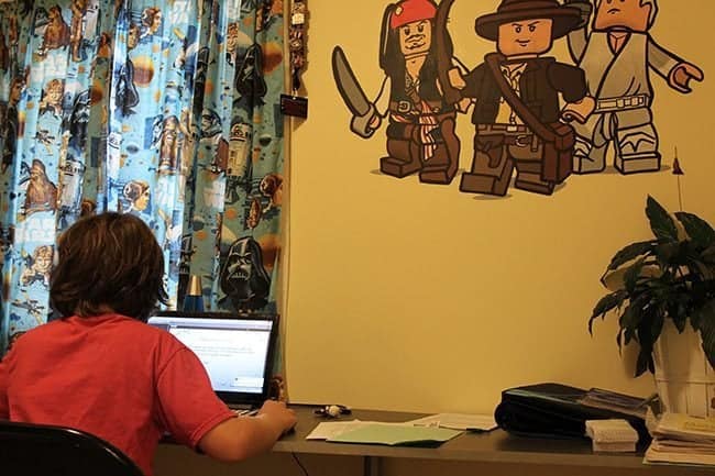 boy sitting, facing the laptop near the yellow painted wall