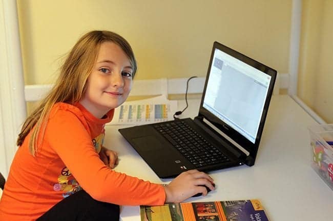 a young girl sitting, facing the laptop and holding the mouse