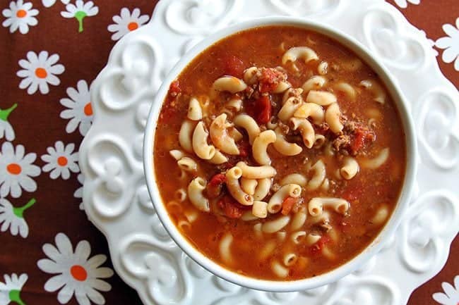 Classic Beef & Tomato Macaroni Soup in a white soup bowl of heart design, red floral tablecloth underneath